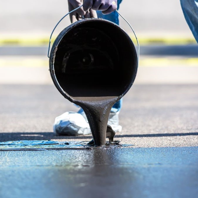 Sealer being poured on top of a concrete driveway.