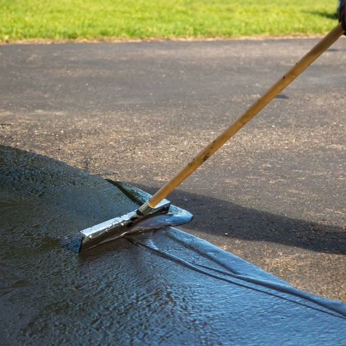 Sealer being spread on a concrete driveway with a broom brush.