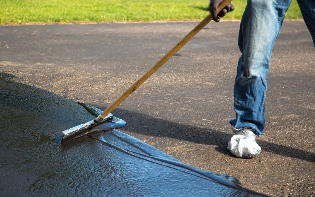 Sealer being spread on a concrete driveway with a broom brush.