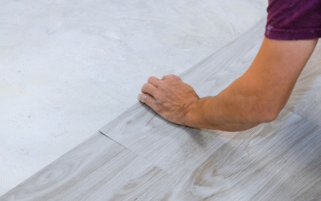 A man laying laminate planks down on a concrete floor foundation.