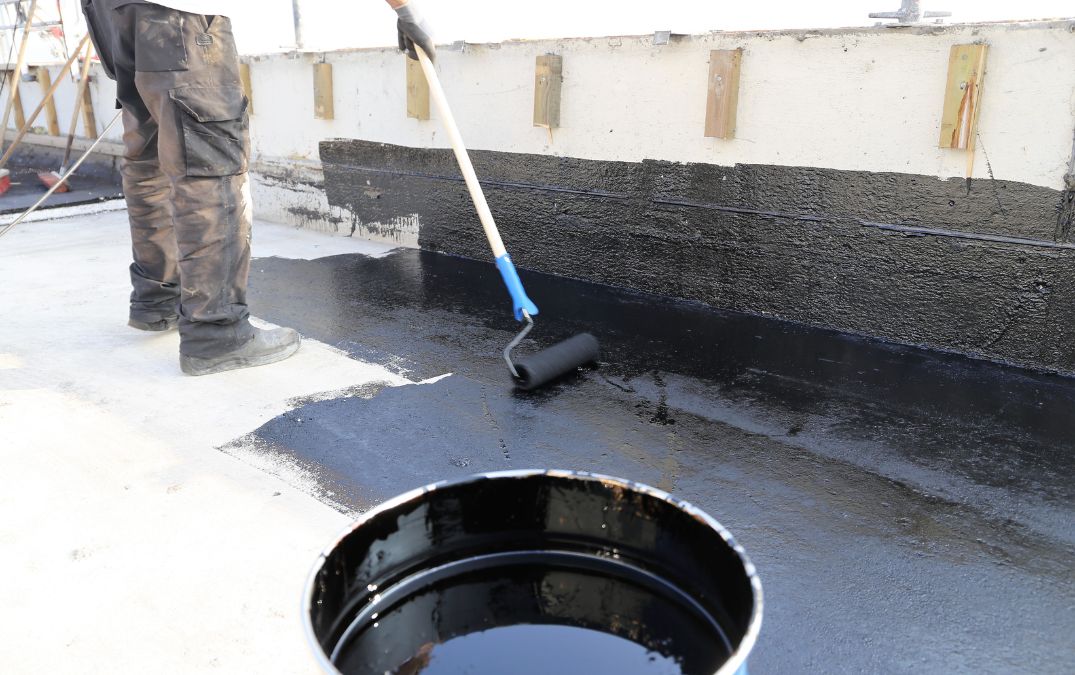 A man applying concrete sealer to a floor outside, using a roller.