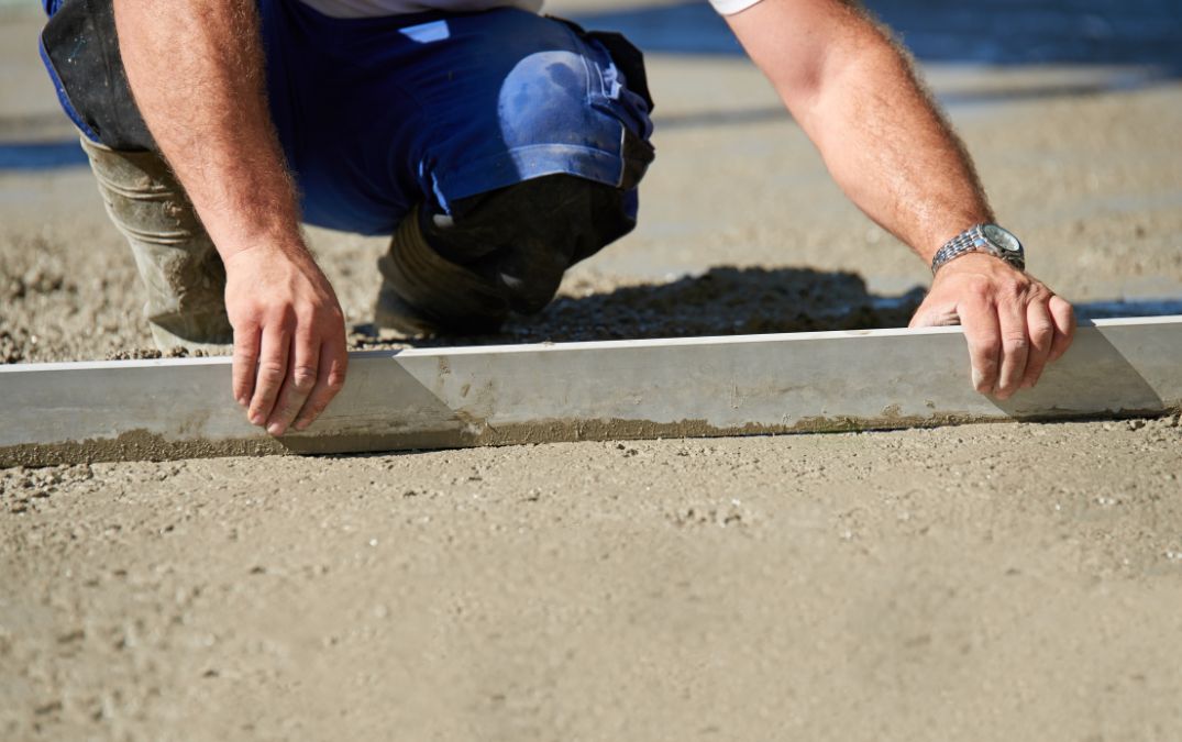 A steel screed board being used to smooth concrete.