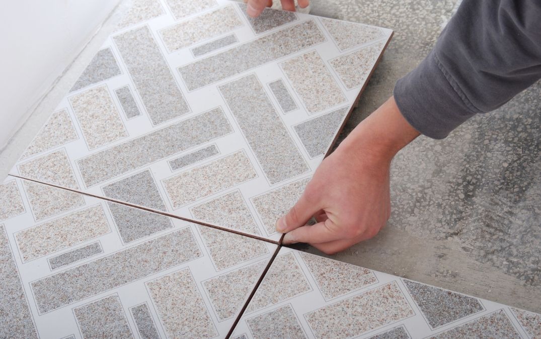 A man laying peel and stick tiles to a primed concrete floor.