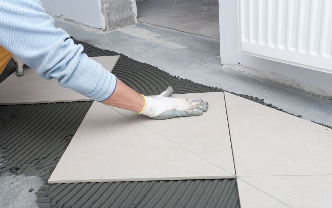 A man laying tiling down on concrete flooring.