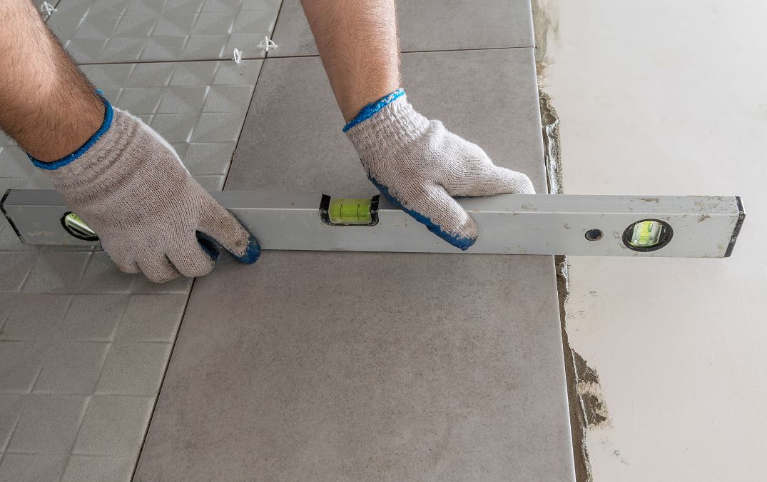 A spirit level being used to level flooring tiles on concrete.