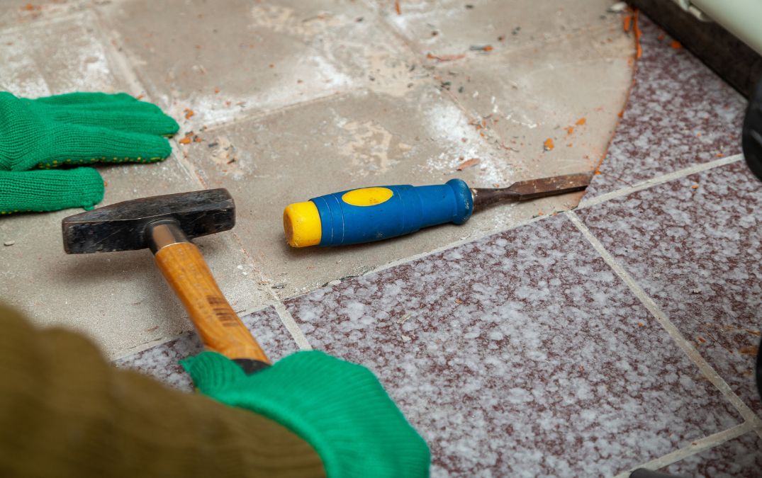 A chisel being hit with a hammer to loosen a tile attached to concrete.