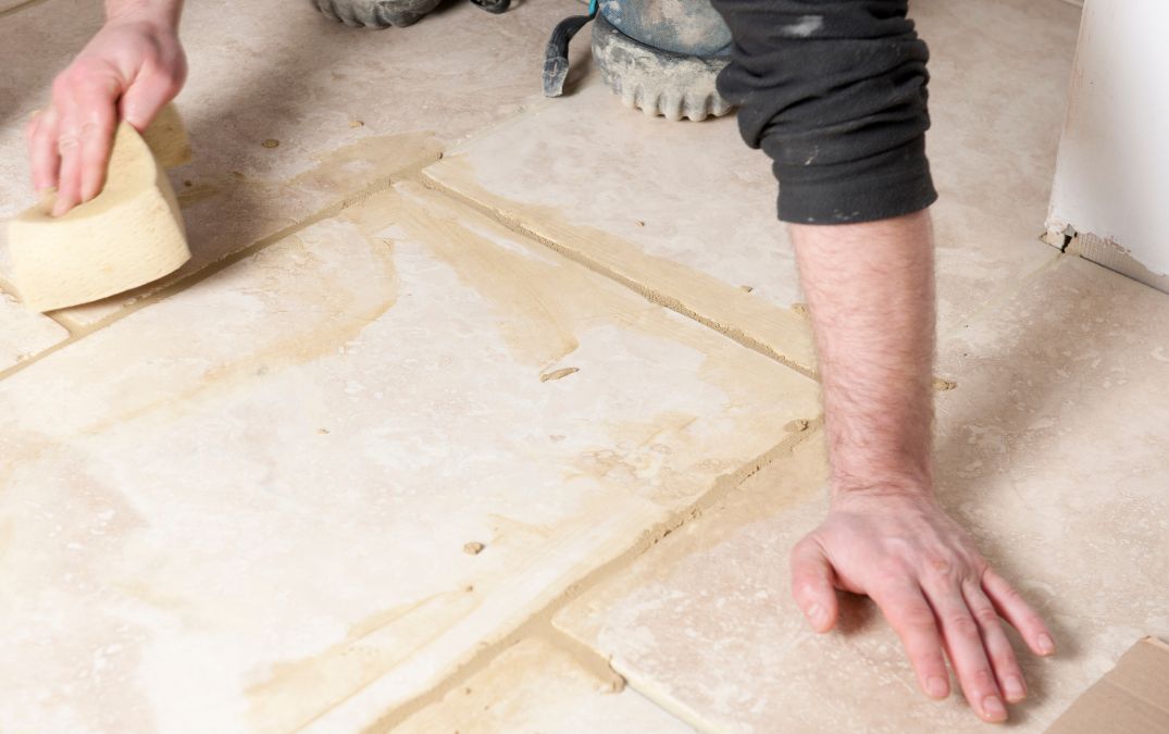 A man using a sponge and chemical cement remove on floor tiles.