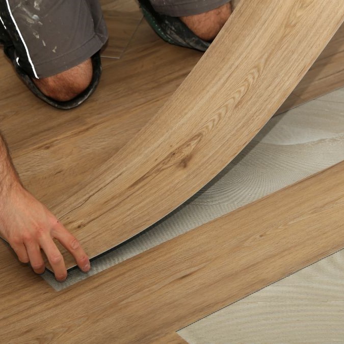 A man laying vinyl flooring onto underlay, atop of concrete.