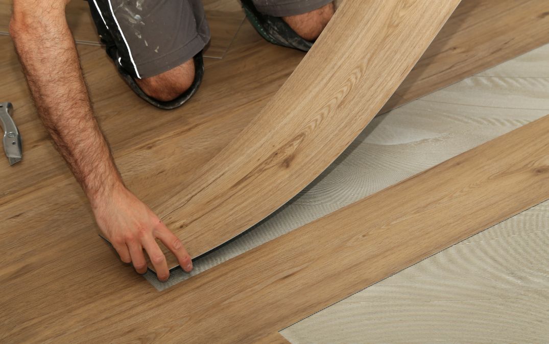 A man laying vinyl flooring onto underlay, atop of concrete.